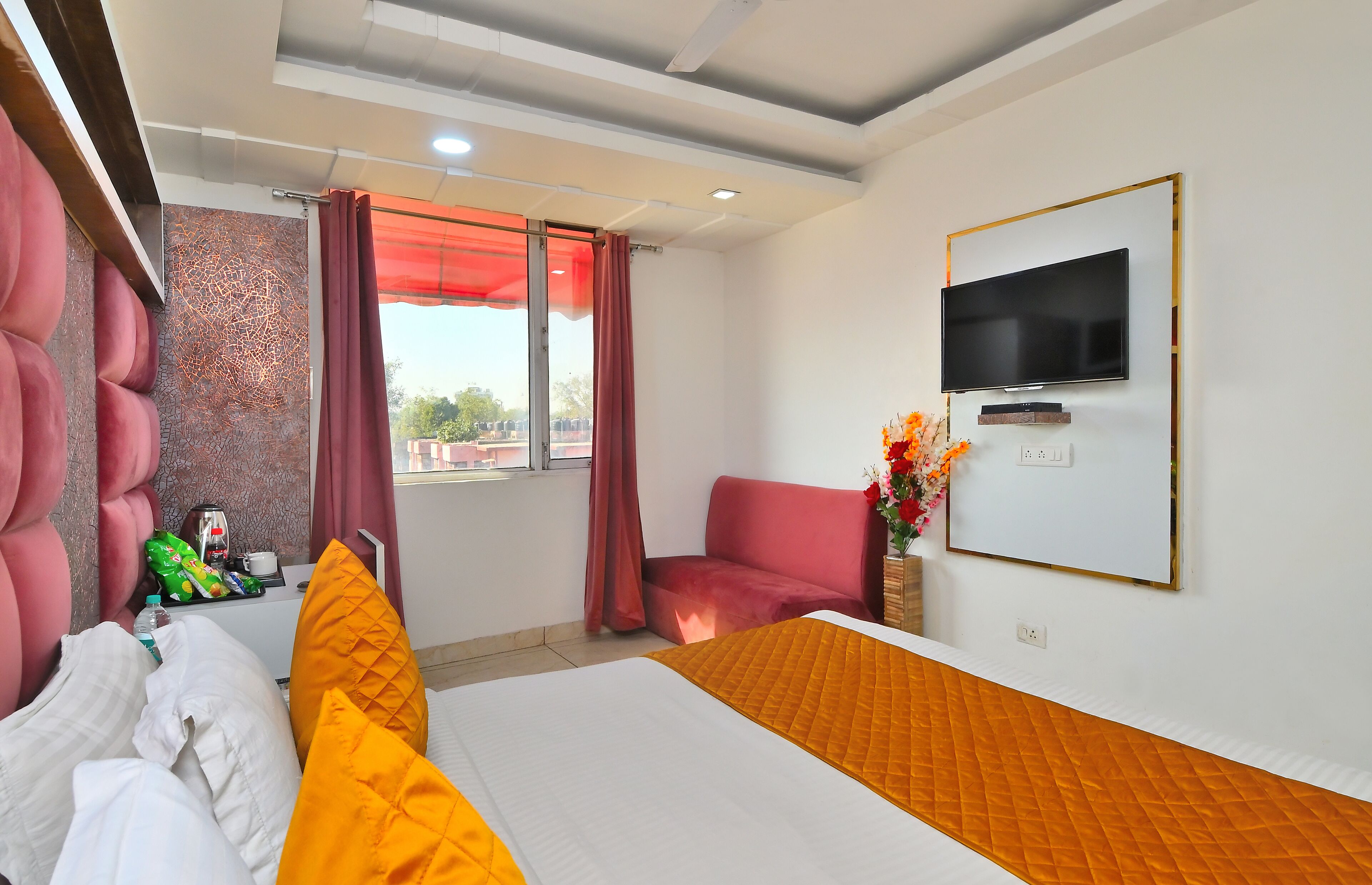 Habitación de hotel con cama, televisor montado en la pared, ventana con cortinas y un sillón rojo.
