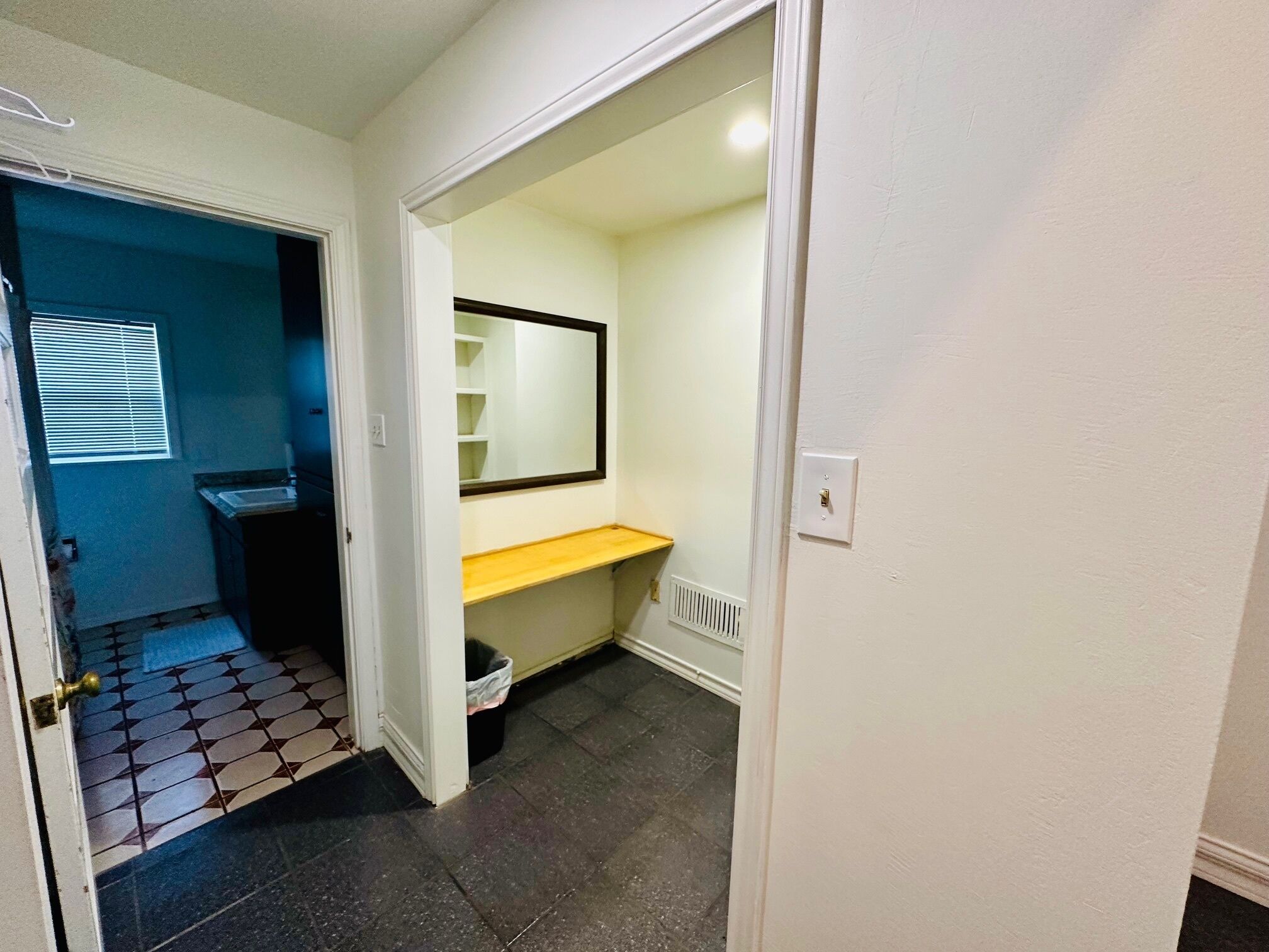A narrow hallway with a tiled floor, a sink, and a mirror on the wall.