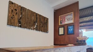 A reception desk with a rustic wooden design, a framed certificate on the wall, and a framed picture above it. - Bali De Pardis Cottage (Munduk)