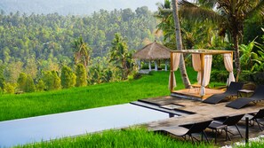 A thatched-roof gazebo with a wooden platform and black lounge chairs, overlooking a lush green rice field and dense tropical forest. - Bali De Pardis Cottage (Munduk)