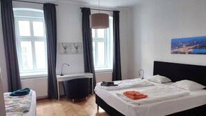 A hotel room with a large bed, a desk, and a chair. There is a window with curtains, a painting on the wall, and a radiator.