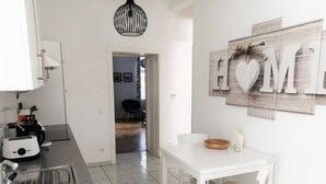 A modern kitchen with a white table and chair, a toaster, and a sink. A 'HOME' sign is on the wall.