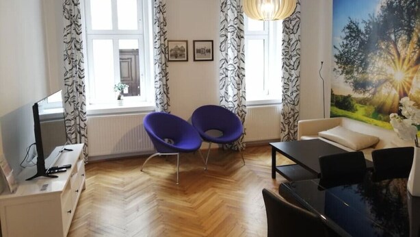 A room with two blue chairs, a dining table, a TV, and a painting on the wall.