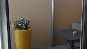 A small balcony with a yellow planter, a metal pole, and a table with a chair. - Cozy 2 bedroom Apart with balcony in Ottakring (Vienna)
