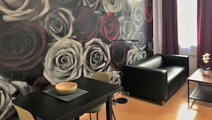 Een moderne woonkamer met een grote bloemenmuur, een zwarte leren bank, een eettafel met een schaal en een klein bijzettafeltje.
