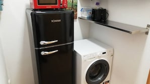 Een compacte kitchenette met een zwarte koelkast, een magnetron en een voorlader wasmachine.