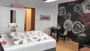 Een slaapkamer met een bed, een bureau en een stoel. Er is een kledingkast en een deur naar een andere kamer.