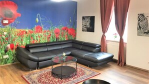 Un salon avec un canapé d’angle en cuir noir, une table basse en verre et une grande fresque murale représentant des coquelicots.