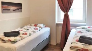 Une chambre avec deux lits, une fenêtre avec des rideaux, un radiateur et un tableau au mur.