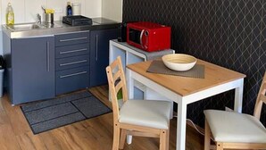 Une cuisine de taille réduite avec des meubles gris, un micro-ondes rouge et une table à manger en bois accompagnée de deux chaises.