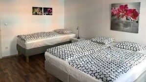 Un dormitorio con dos camas individuales, una cama grande y una mesita de noche con lámpara.