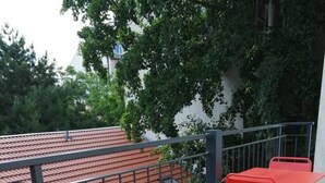 Una terraza en la azotea con mesas y sillas de metal rojo, una baranda metálica y vistas a árboles y edificios.