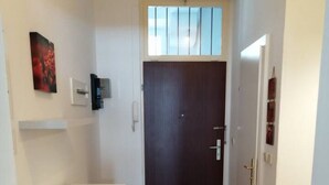 A narrow hallway with a wooden floor, a dark wooden door at the end, a white cabinet on the left, and a small rug in the center. - Studio Apartment near Reumanplatz (Vienna)
