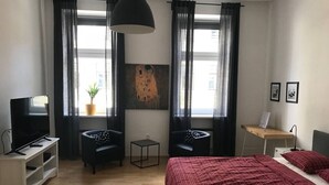 A modern hotel room with a bed, two armchairs, a TV, a small table, and a painting on the wall. - Studio Apartment near Reumanplatz (Vienna)