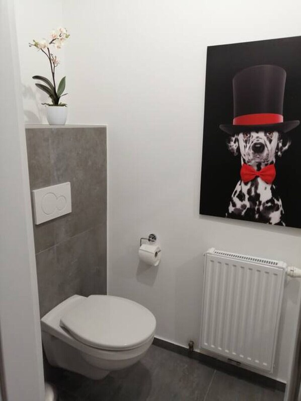 Une salle de bain moderne avec des toilettes, un radiateur et un tableau représentant un dalmatien portant un chapeau haut de forme et un nœud papillon.