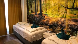 Une chambre avec deux lits, une fresque murale sur le thème de la forêt et une lampe suspendue.