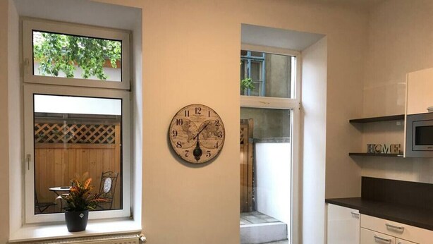 Une cuisine avec une horloge, une plante en pot et une vue sur un balcon.