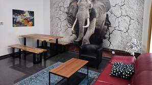 Une pièce dont un mur est orné d’une grande fresque représentant un éléphant, avec un canapé rouge, une table en bois et une chaise noire.