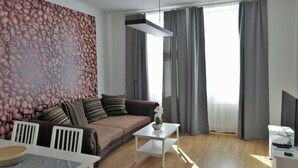 A modern living room with a brown sofa, white chairs, a coffee table, and a TV stand. - Home Apartment near Huberpark (Vienna)