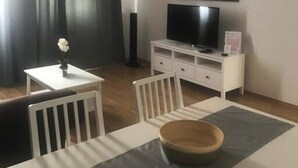 A modern living room with a dining area, featuring a flat-screen TV, white furniture, and a world map artwork. - Home Apartment near Huberpark (Vienna)