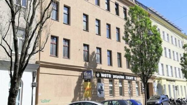 A multi-story building with a beige facade, several windows, and a sign for 'MOTO PSYCHO TIGHT'. - Home Apartment near Huberpark (Vienna)