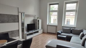 Una sala de estar moderna con un sofá gris, una mesa de comedor con sillas, un televisor y una unidad de estanterías empotradas.