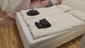 Una cama bien hecha con un colchón blanco y una cubierta con motas, acompañada de dos toallas oscuras dobladas.