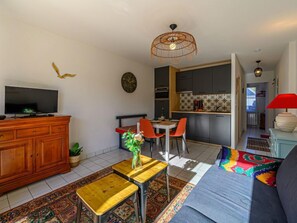 Ein modernes Wohnzimmer mit Fernseher, Holzschrank und Essbereich mit Stühlen und Tisch.
