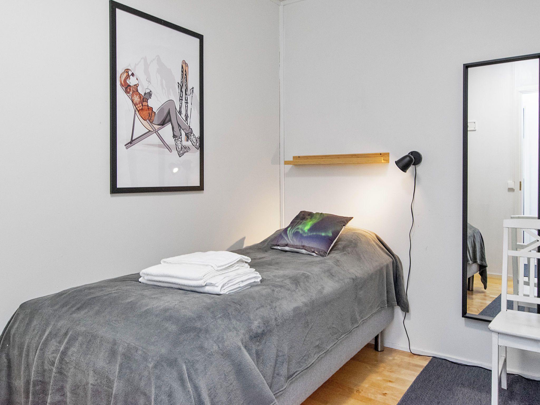Un dormitorio con cama, escritorio, silla, un cuadro en la pared y una lámpara de noche.