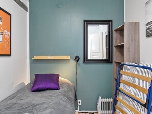 A bedroom with a bed, a pillow, a bedside lamp, a radiator, and a mirror on the wall.