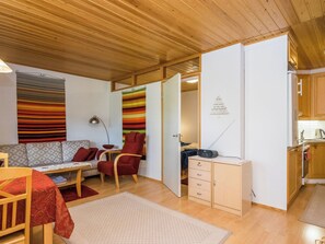 Un espacio habitable compacto con sofá, una silla roja, una mesita, un armario y una zona de kitchenette.