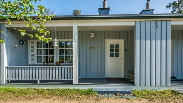 A single-story building with a porch, a white door, and a chimney.