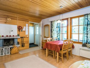 A cozy room with a wooden ceiling, a fireplace, a dining table with chairs, and a window with patterned curtains. - Saariseläntie 8 e 3 by Interhome (Inari)