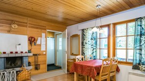 A cozy dining area with a wooden table set for four, a fireplace, and a view through large windows.