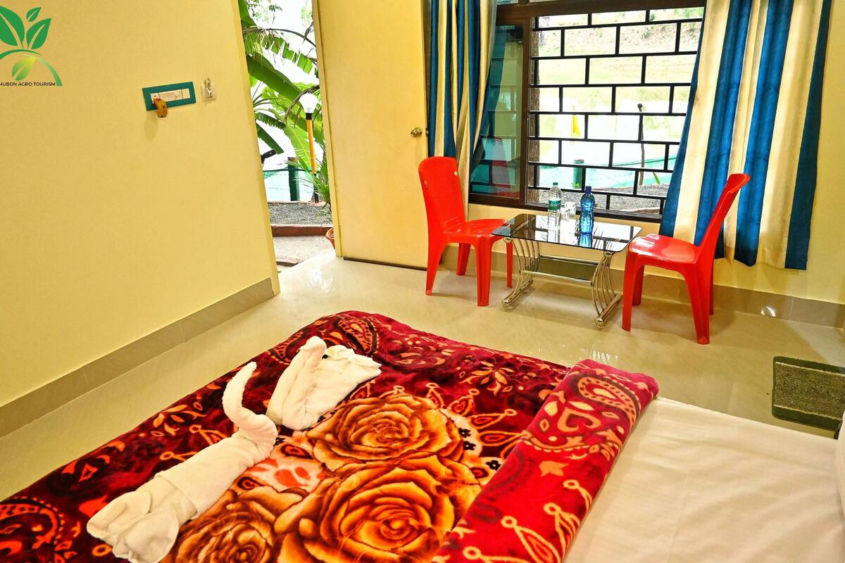 Une chambre d’hôtel avec un lit, deux chaises rouges, une petite table et une fenêtre avec des rideaux.