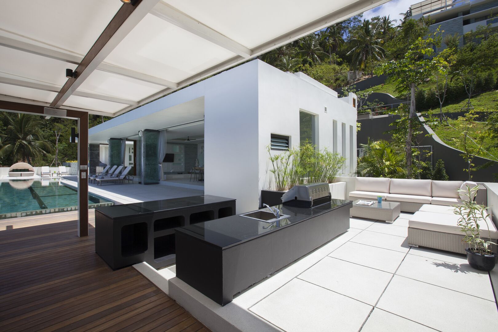 Ein moderner Außenbereich mit Pool, einer integrierten Kücheninsel und einer Sitzecke mit Sofa und Sesseln.