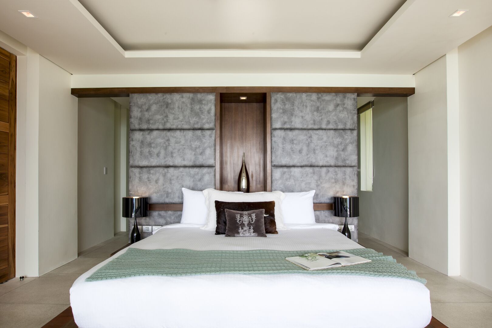 A modern hotel bedroom with a large bed, two bedside tables, and a unique textured wall behind the bed.