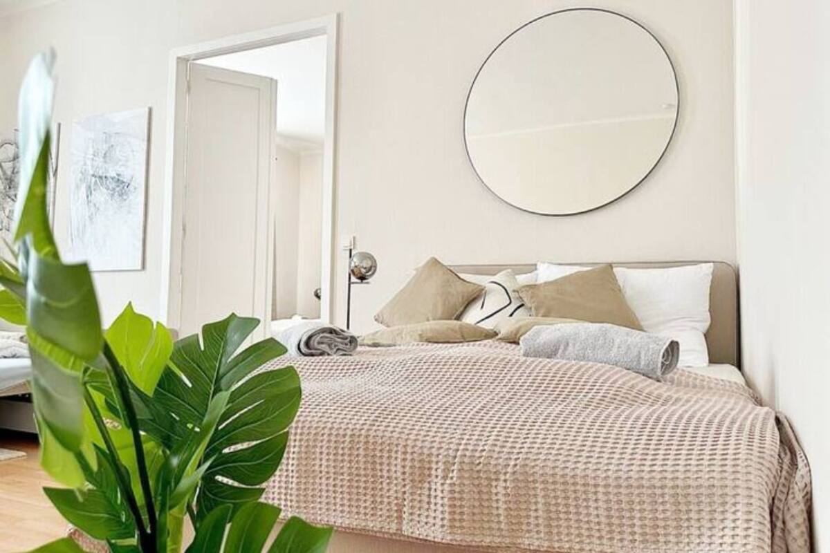 A bedroom with a bed, a round mirror, and a plant.