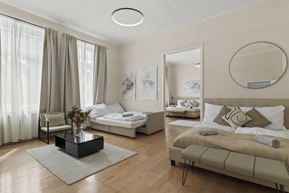 A modern hotel room with a large bed, a sofa, a coffee table, and a dining area.