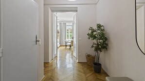 A hallway with a wooden floor, a potted plant, a bench, and a door leading to a dining area. - Belvedere Apartments (Vienna)