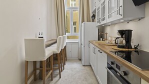 A compact kitchen with a dining area, a refrigerator, a coffee maker, and a window with curtains. - Belvedere Apartments (Vienna)