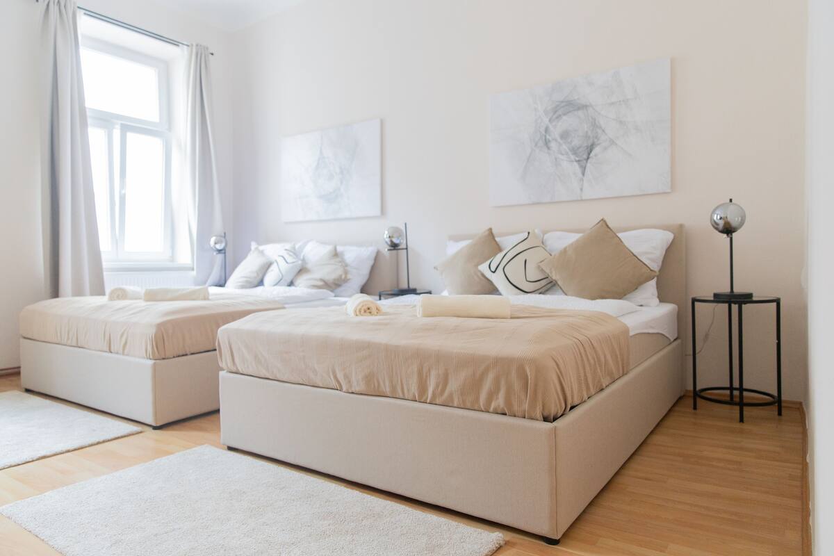 A modern bedroom with two beds, a bedside table, a floor lamp, and artwork on the walls.