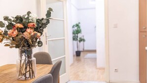 A dining area with a wooden table and chairs, a vase with flowers, and a view into a room with a plant. - Belvedere Apartments (Vienna)