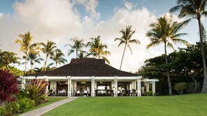 A covered outdoor seating area with tables and chairs, surrounded by palm trees and greenery. - Golf Course Front - Upgraded - Kulalani Mauna Lani (Waimea)