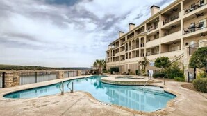A swimming pool with a curved design, surrounded by a stone deck and a stone wall. - Puerto Azul - The Island at Lake Travis (Lago Vista)