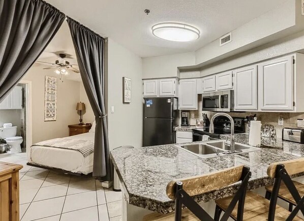 A compact kitchen with white cabinets, a granite countertop, and a built-in microwave.