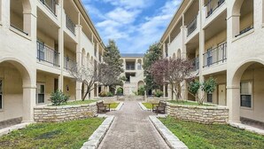 A courtyard with a central pathway flanked by buildings with balconies and stone walls. - Puerto Azul - The Island at Lake Travis (Lago Vista)