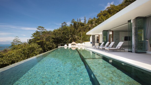 A modern infinity pool with clear water, surrounded by lush greenery and a view of the ocean.