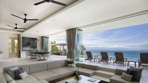 A modern living room with a large sectional sofa, a dining area, and a balcony with ocean views.