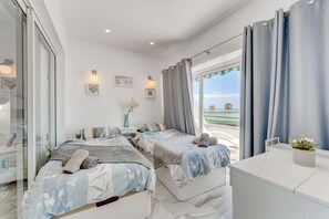 Two single beds with floral-patterned bedding, a bedside table, and a nightstand with a lamp, set against a backdrop of framed artwork and a decorative vase.